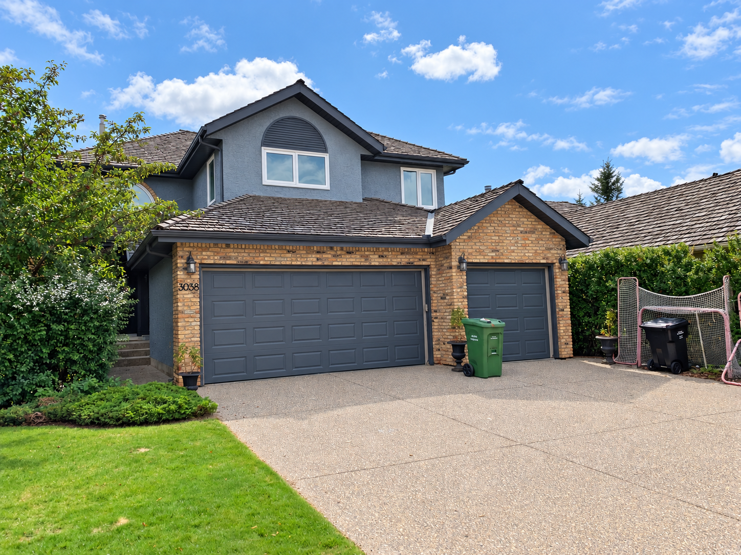 Completed Signal Hill exterior with blue-grey stucco, black soffits and dark garage doors beside existing brickwork.