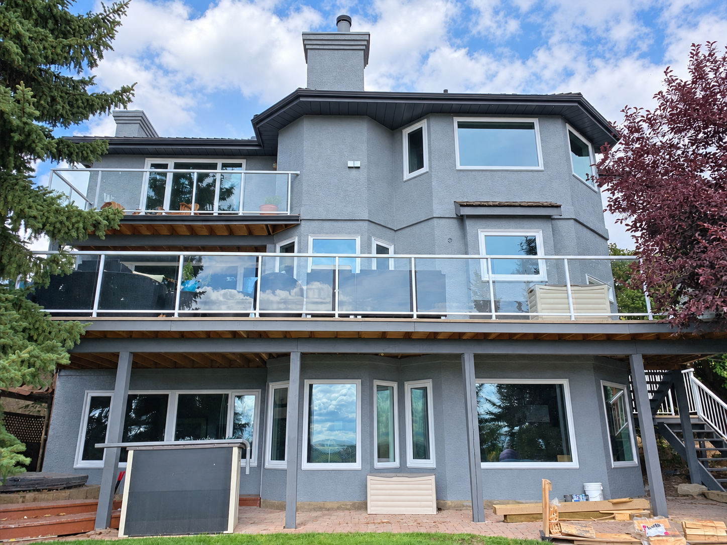 Rear of the Signal Hill home with blue-grey stucco, black soffits, white window frames and glass deck railings.